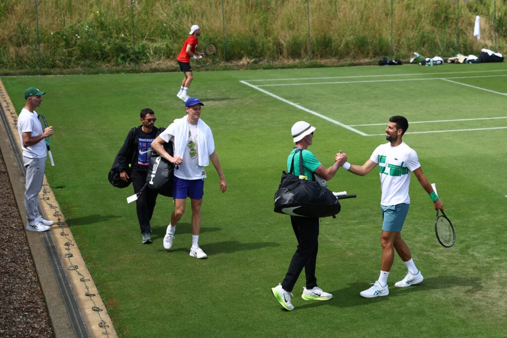 Novak Djokovic of Serbia greets Darren Cahill, the coach of Jannik Sinner of Italy on court after a practice session at Aorangi Park during previews prior to The Championships Wimbledon 2025 at All England Lawn Tennis and Croquet Club.