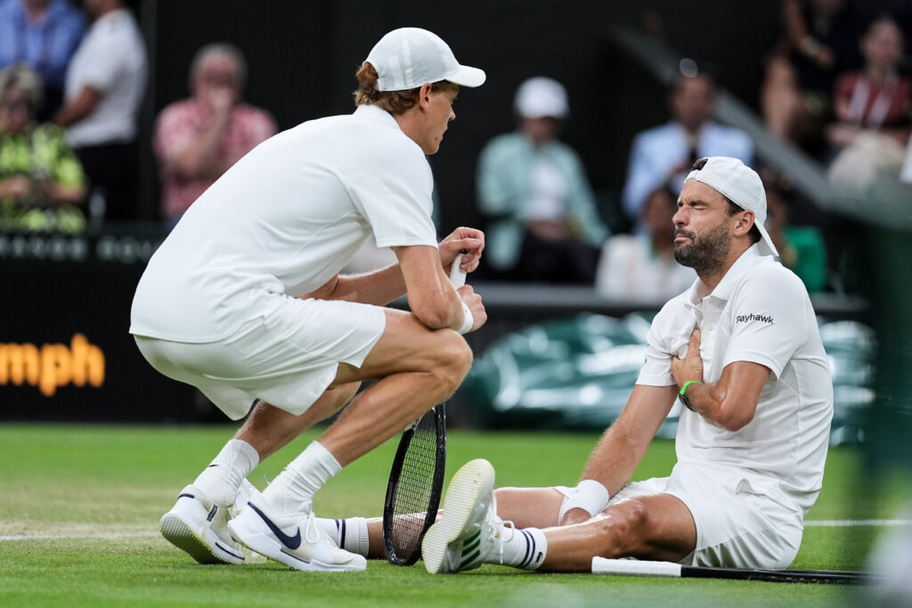 Jannik Sinner crouches beside an injured Grigor Dimitrov