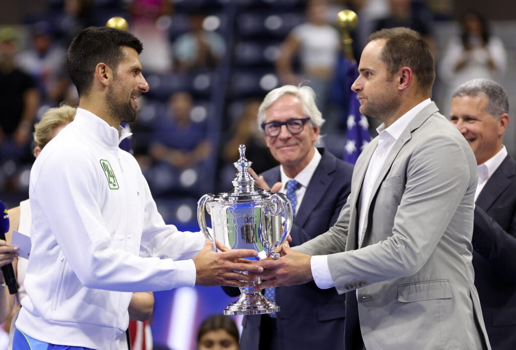 Novak Djokovic of Serbia receives his winners trophy from Andy Roddick after defeating Daniil Medvedev of Russia during their Men's Singles Final match on Day Fourteen of the 2023 US Open at the USTA Billie Jean King National Tennis Center.