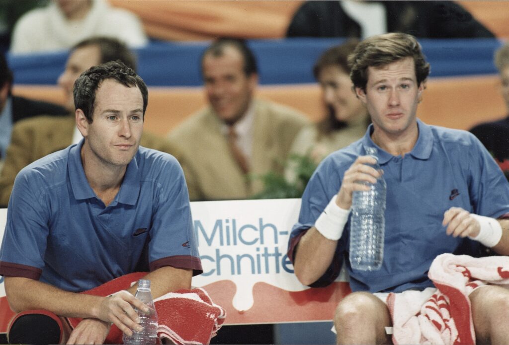 John McEnroe and Patrick McEnroe sat on bench together during doubles match in Stuttgart.