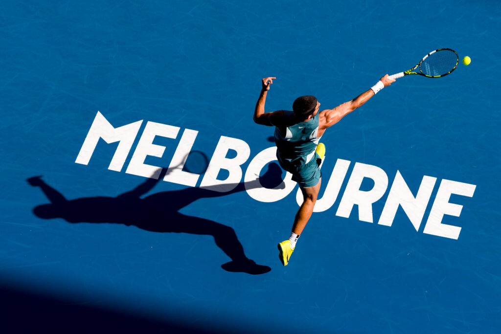 Carlos Alcaraz hits a forehand whilst stood on the Melbourne sign