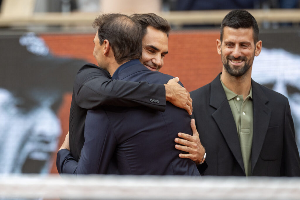 Rafael Nadal and Roger Federer hug as Novak Djokovic looks on Court Philippe-Chatrier at the 2025 French Open.