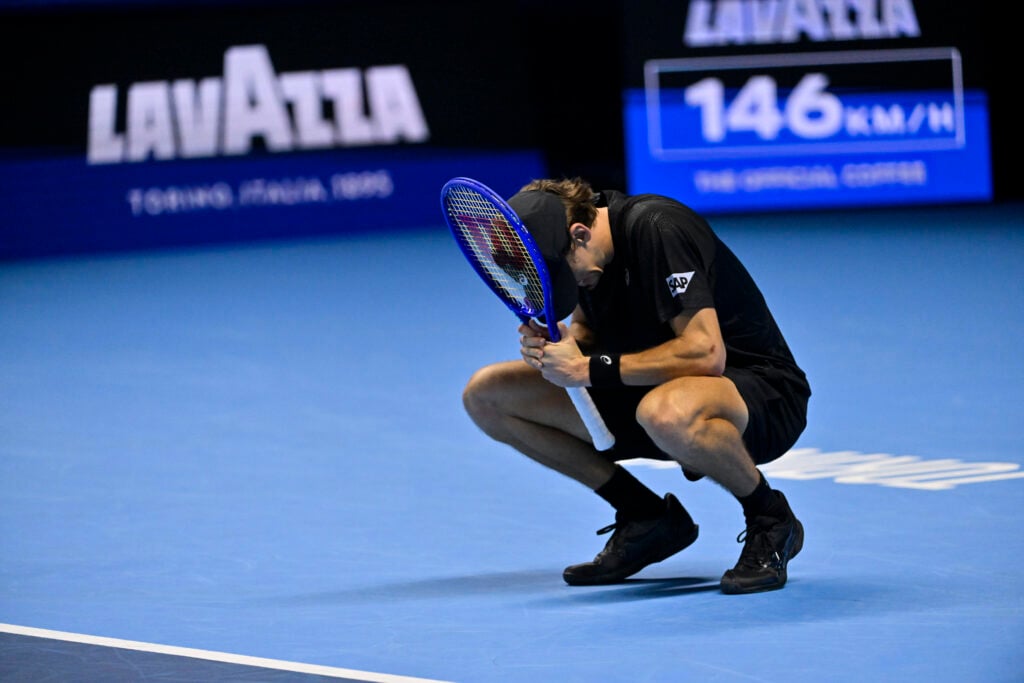 Alex de Minaur crouches, resting his head on his racket, looking dejected