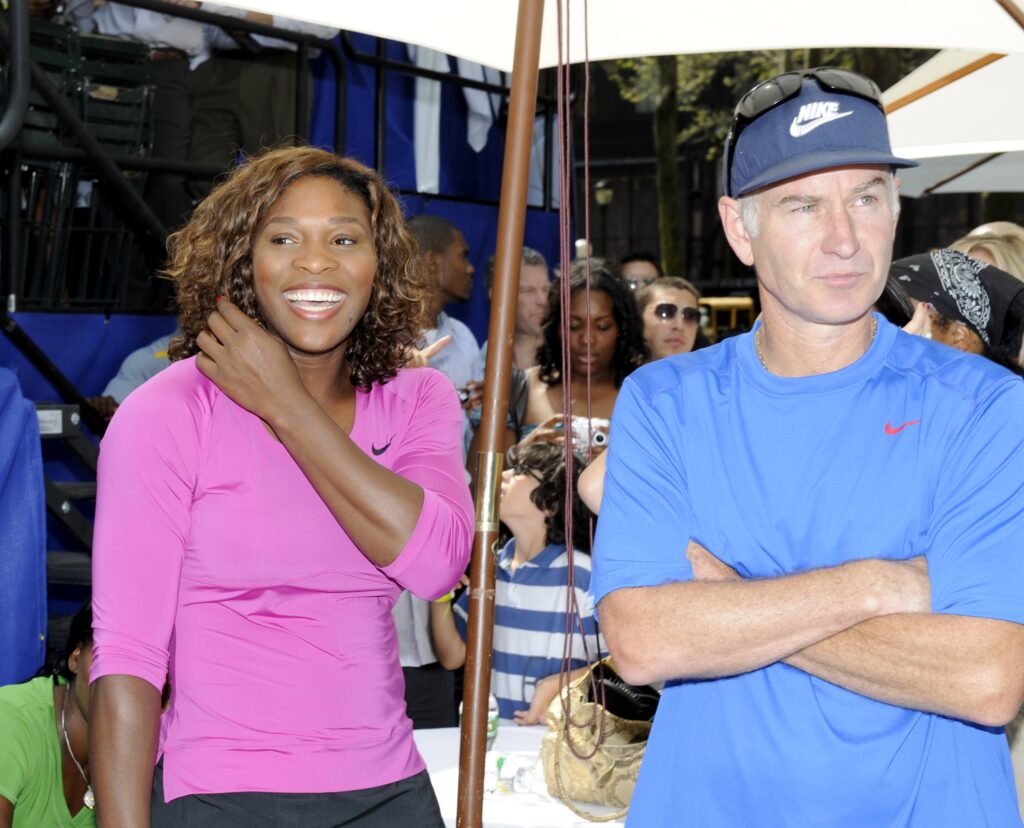 Serena Williams laughs and John McEnroe, arms crossed, stand side by side