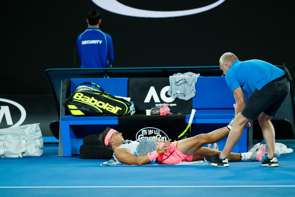 Rafael Nadal, lying courtside, receives treatment for an injury