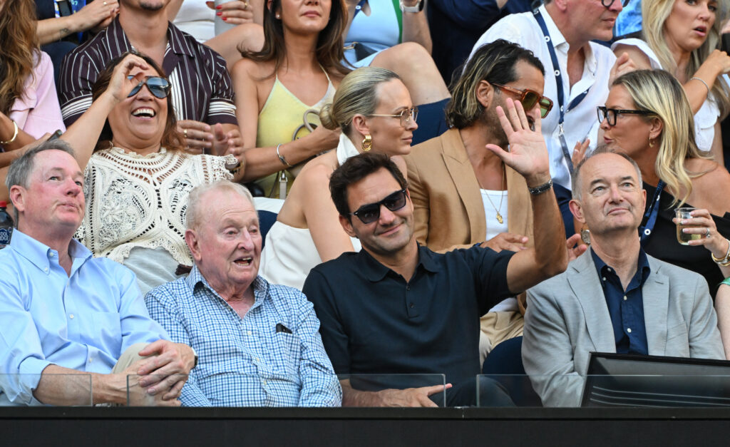 Roger Federer waves whilst sat next to Rod Laver