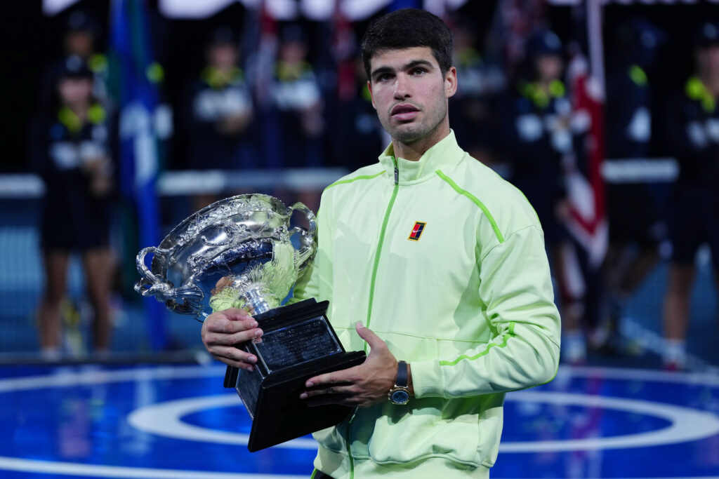 Carlos Alcaraz holding the Norman Brookes Challenge Cup after beating Novak Djokovic to win the 2026 Australian Open.