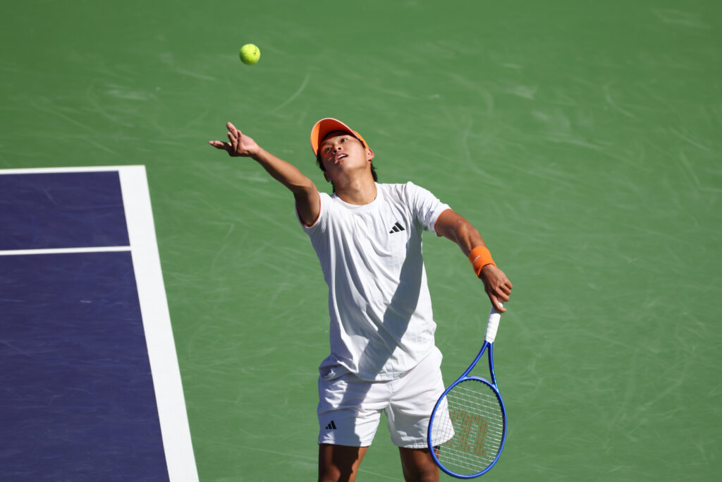 Learner Tien hits a serve against Ben Shelton at Indian Wells in 2026.