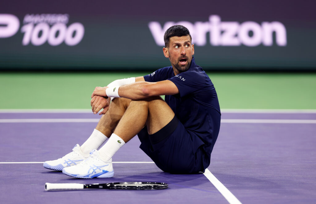 Novak Djokovic sits on the court during his match against Jack Draper at Indian Wells in 2026.
